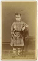 Portrait of a young boy in a plaid dress with pockets and striped leggings