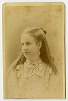 Portrait of a woman with long curly hair, dnagling earrings, and a white bow on her collar
