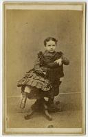 Portrait of a child in a dark plaid dress posing on a stuffed tassled chair