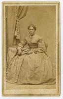 Portrait of a woman with dark skin and a top bun resting her arm on a table with a book