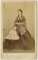 Photo of a standing woman with a gingham shawl posing with an infant on a chair