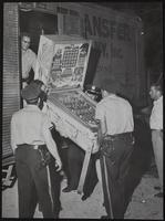 Officers unload part of loot. Loot taken from truck by deputy Don Hallmark. Also from left are Earl Harris, Virgil Foust, Don Andrews, Dt. Dick Stanwix, and Eugene Williams. 22 machines were taken in raid on local businesses.