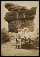 Unidentified Women on donkeys in front of rock formation