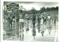 Student officials, photographers, athletes standing on a wet track