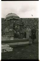 Two men standing on a stage on the track field with two other men standing nearby.