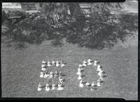 Women sitting on grass in the shape of the numbers 50