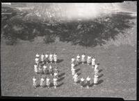 Women standing on grass in the shape of the numbers 50
